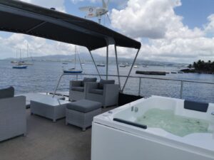 the upper deck of the houseboat with its lounge, a hot tub, and a view of the bay of Fort-de-France and Mount Pelée
